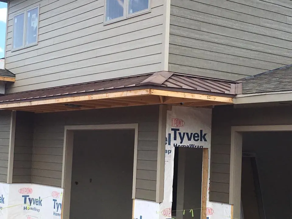 New residential home build with unfinished dark taupe siding and brown steel roof