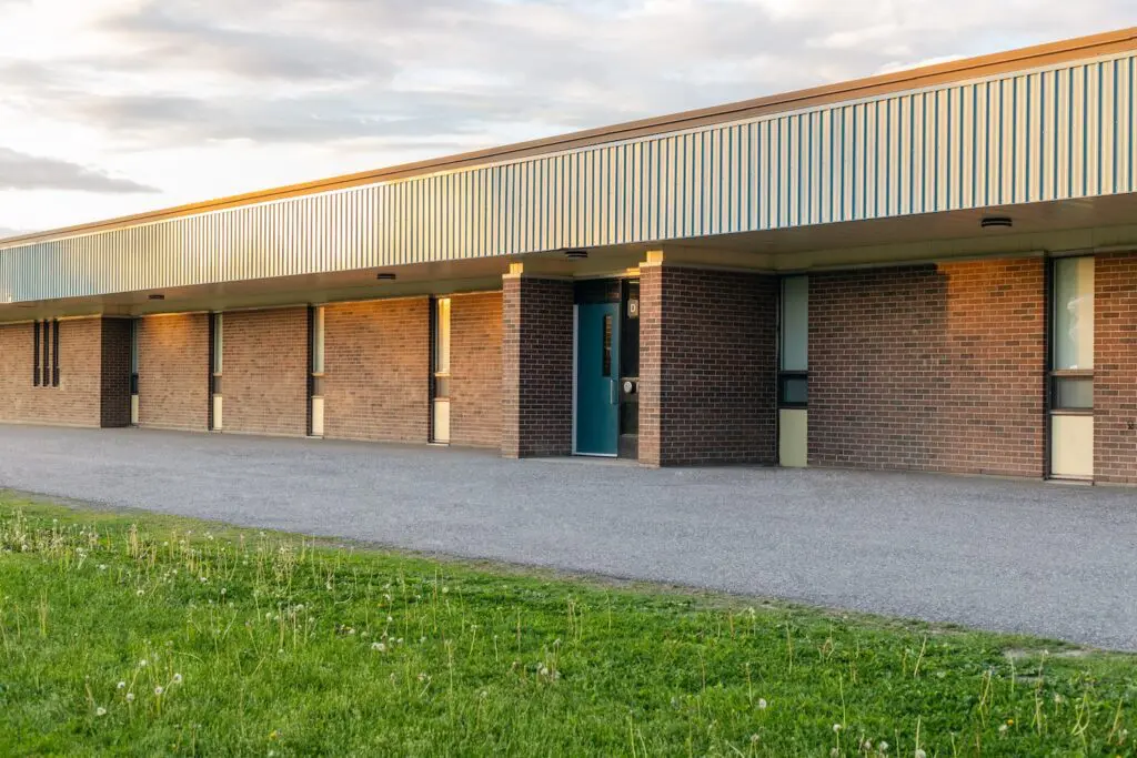 School building exterior and schoolyard with green grass in front on a sunny evening.