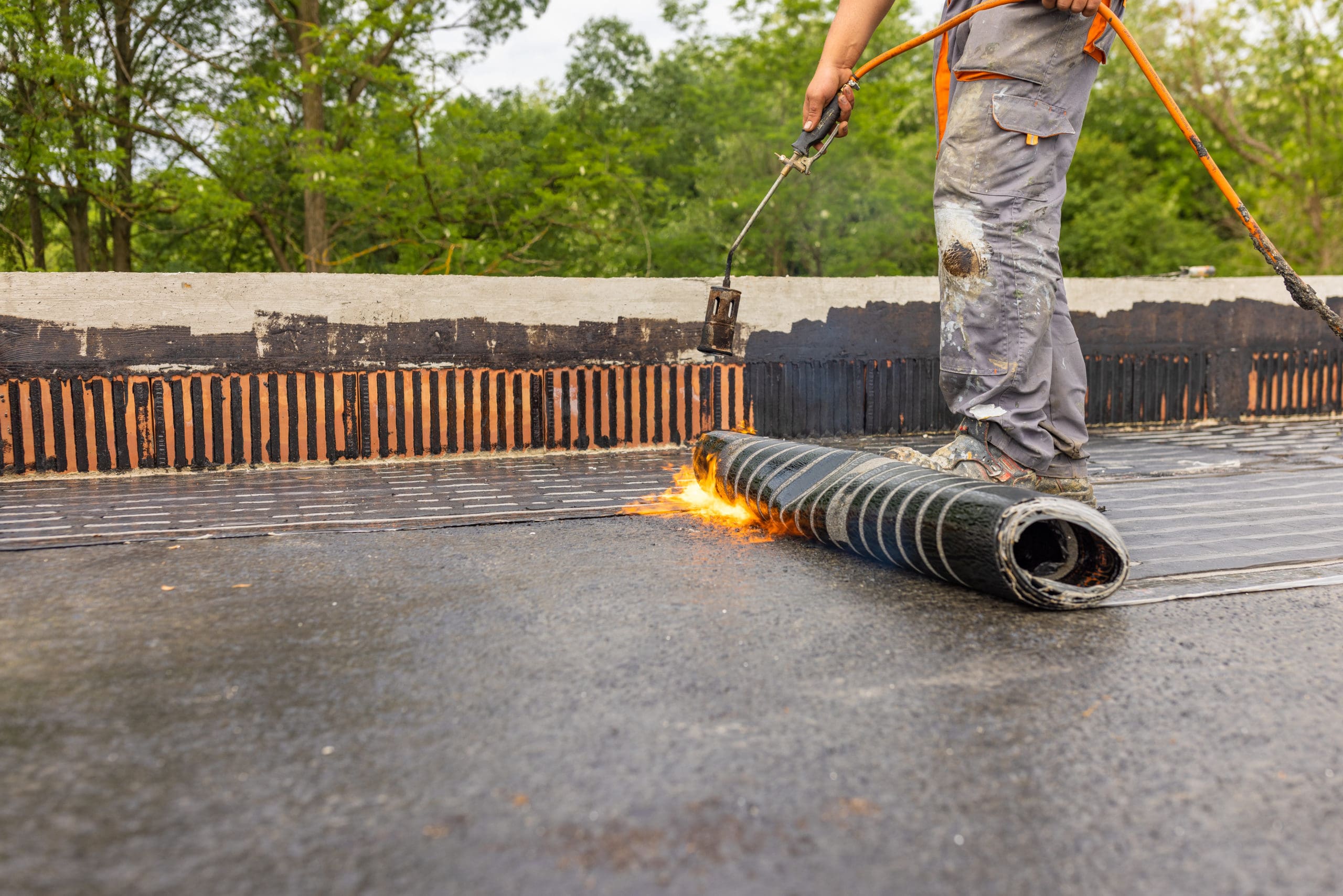 Roofers on Black Flat Roof doing residential roofing work putting down Bituminous Membrane for waterproofing