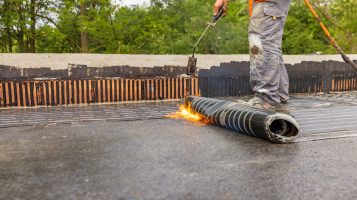 Roofers on Black Flat Roof doing residential roofing work putting down Bituminous Membrane for waterproofing