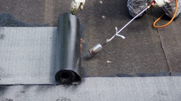 Flat roof installation with propane blowtorch during construction works with roofing felt Roofer using blowtorch for commercial flat roof installation